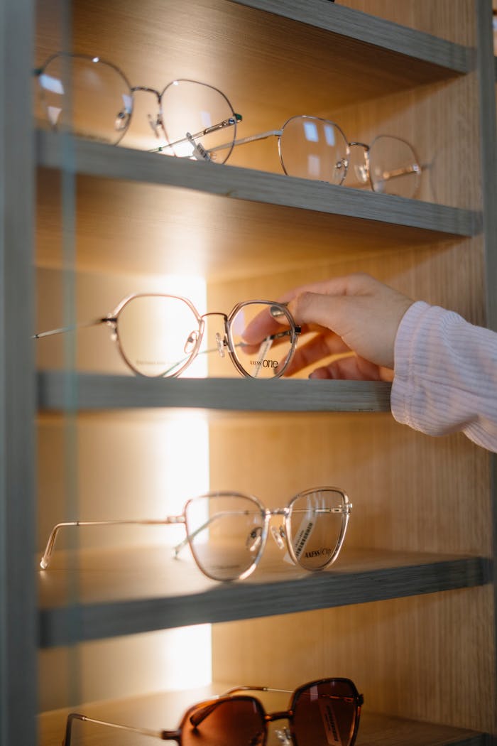 A hand picking glasses from an illuminated display shelf in a store.